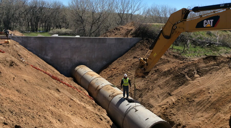 man standing on large pipe in dirt